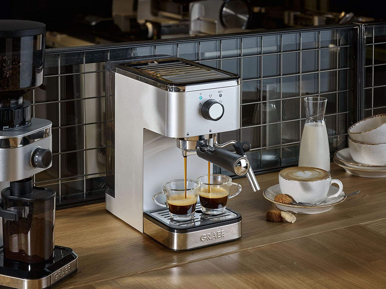 Ekspres do kawy nalewający kawę do dwóch szklanek. Obok filiżanka kawy i ciastka.