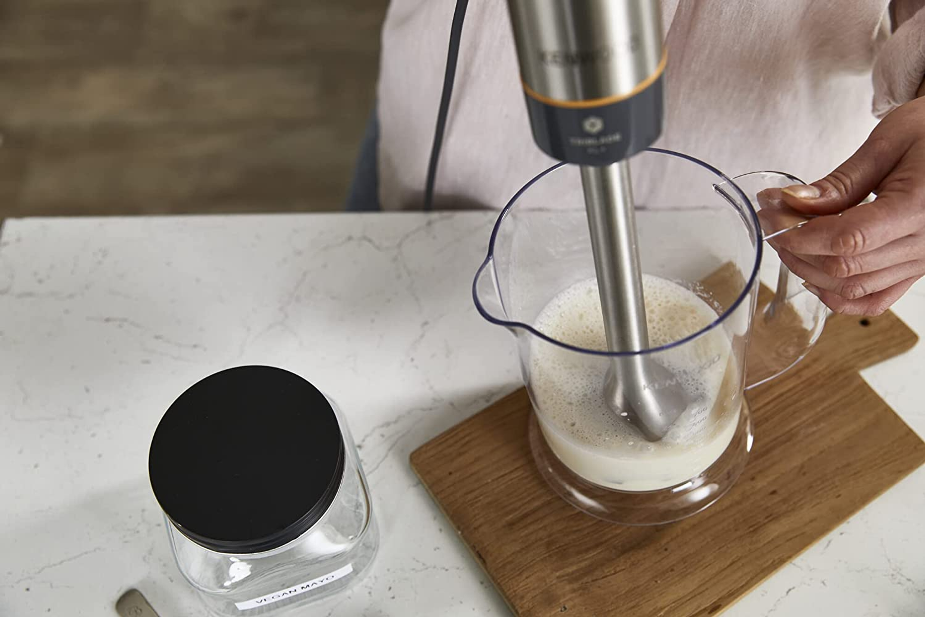 Ręka trzymająca blender ręczny w szklanym dzbanku. Blender miesza ciecz.