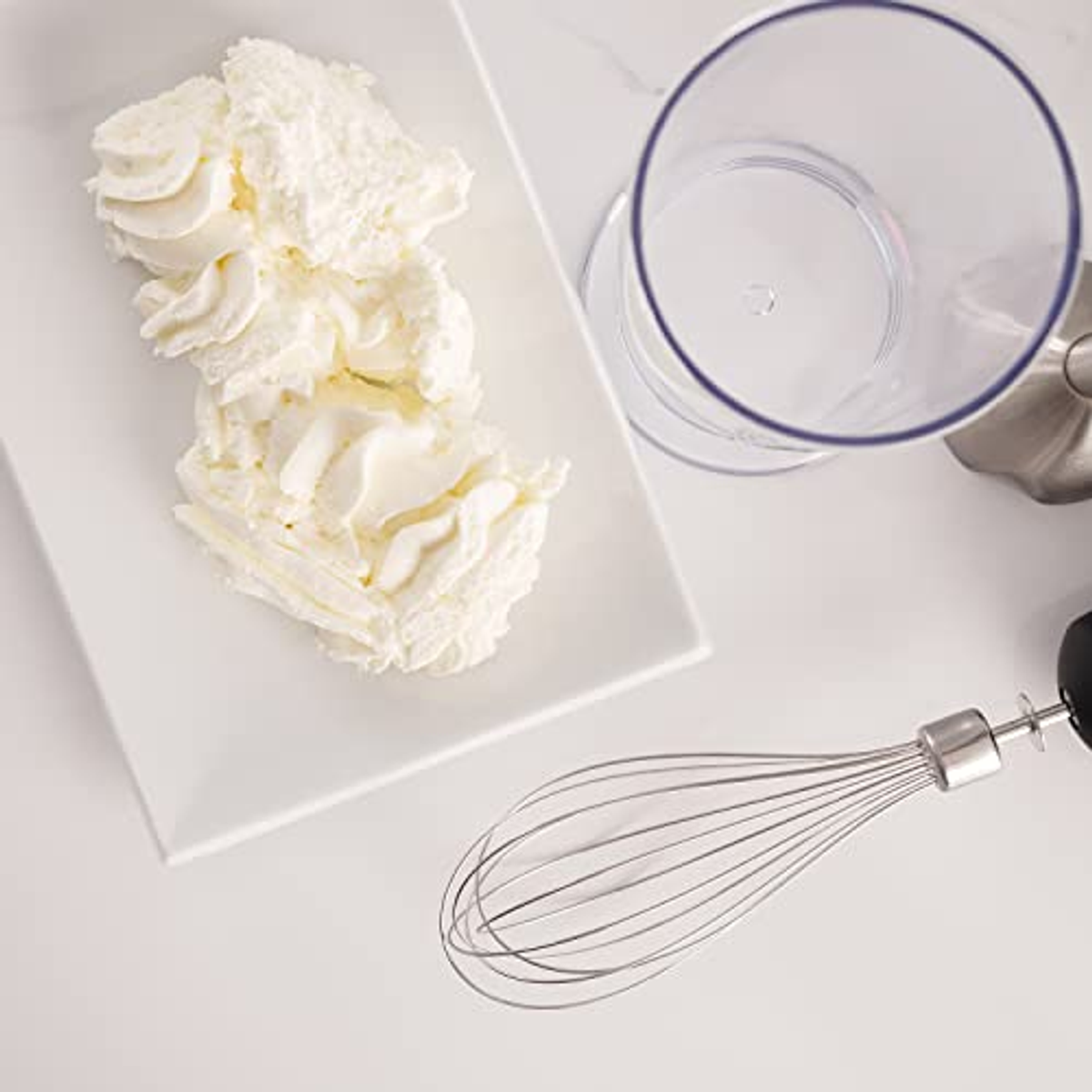 Crema batida en plato blanco. Un batidor a la derecha y un vaso de licuadora transparente detrás.