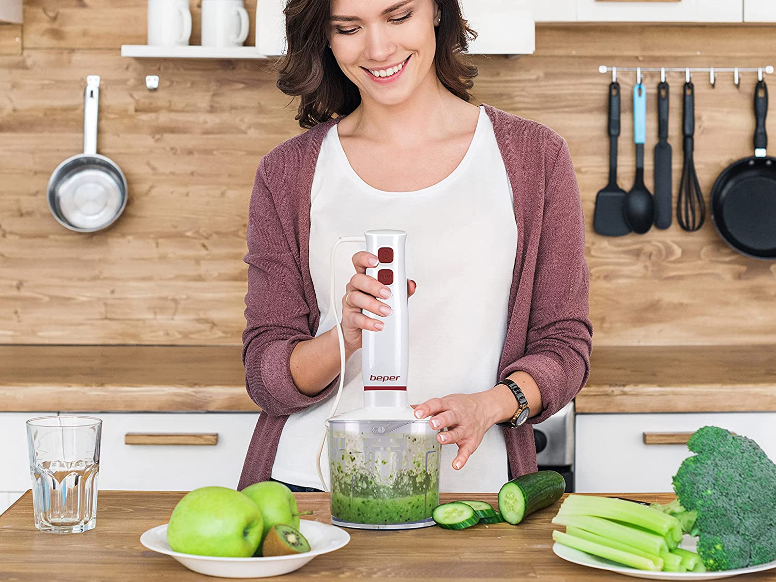 Donna che frulla cibo con un frullatore a immersione in cucina. Ci sono frutta e verdura.