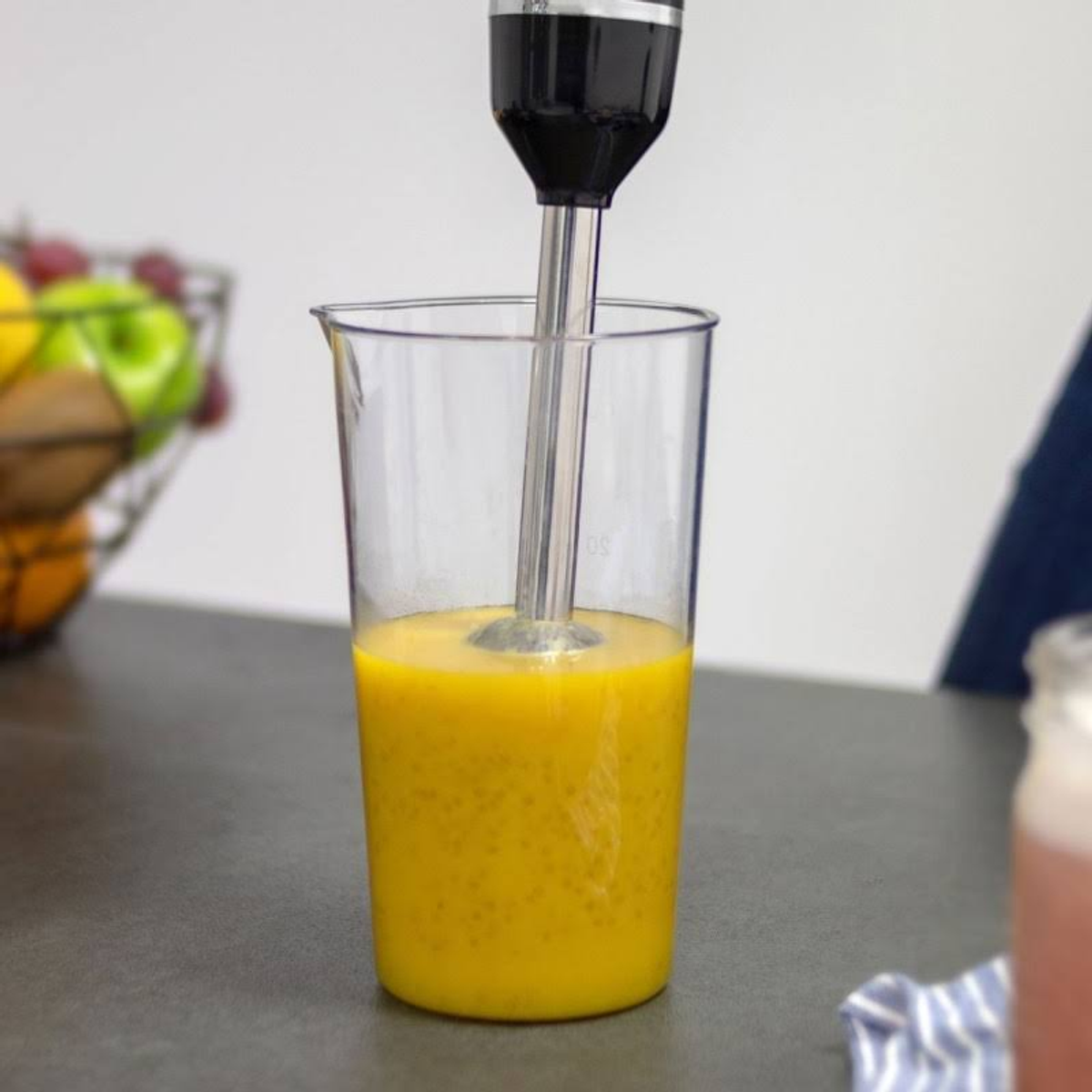 Frullatore a immersione in un becher trasparente con liquido arancione. Il frullatore è nero e argento.