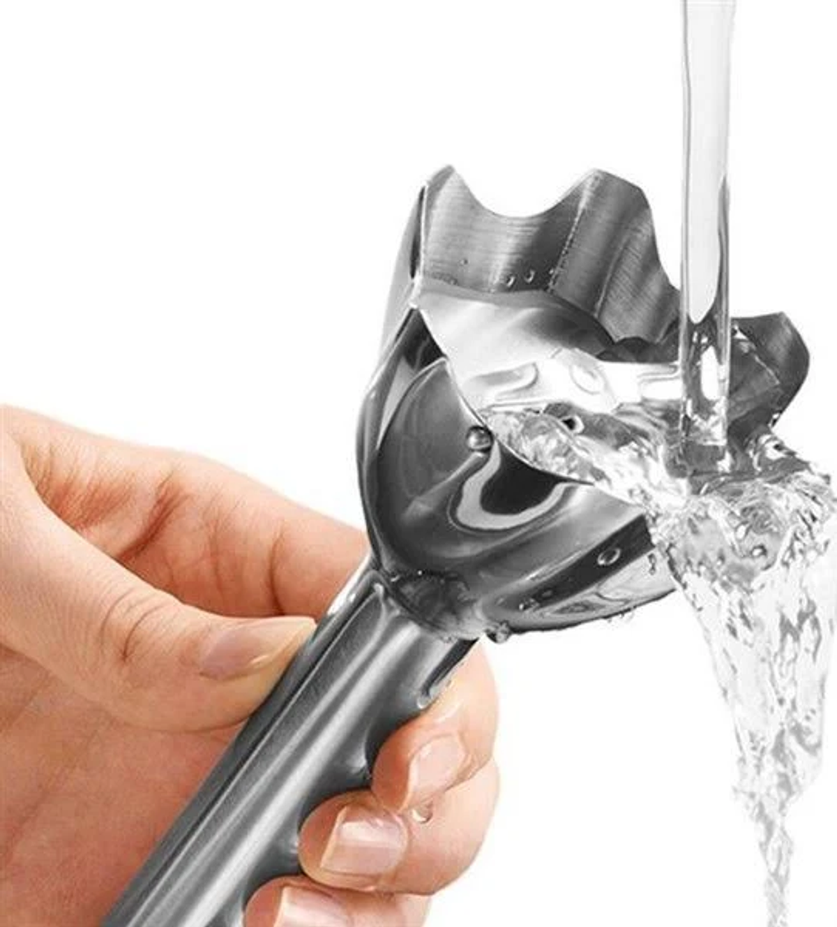 Mano che tiene la testa del frullatore a immersione. Acqua che ci scorre sopra, sfondo bianco.
