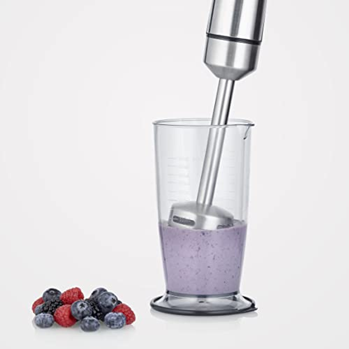 Een staafmixer in een glas met een paars mengsel. Bessen liggen voor het glas.