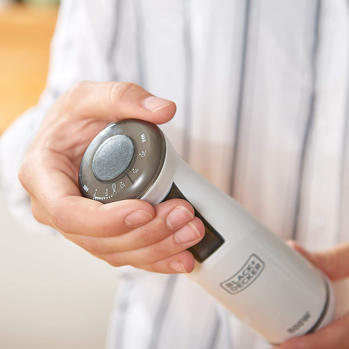 Osoba trzymająca biało-szary blender z pokrętłem, ujęcie z bliska.