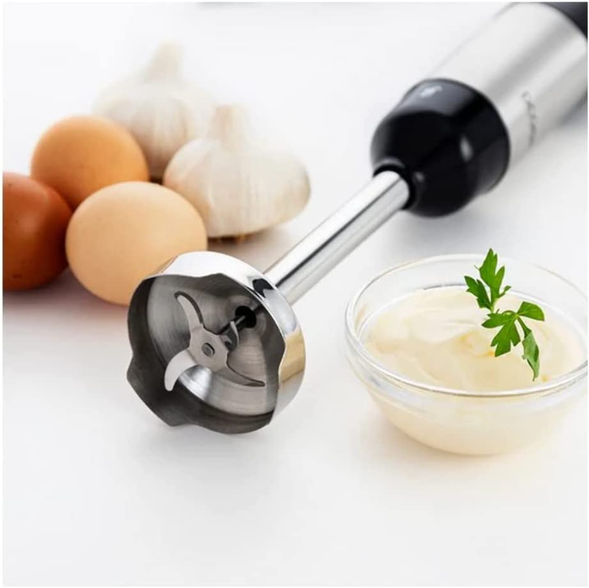 Handlicher Mixer mit Zutaten: Eier, Knoblauch, Mayonnaise in einer Glasschüssel, Petersilie.
