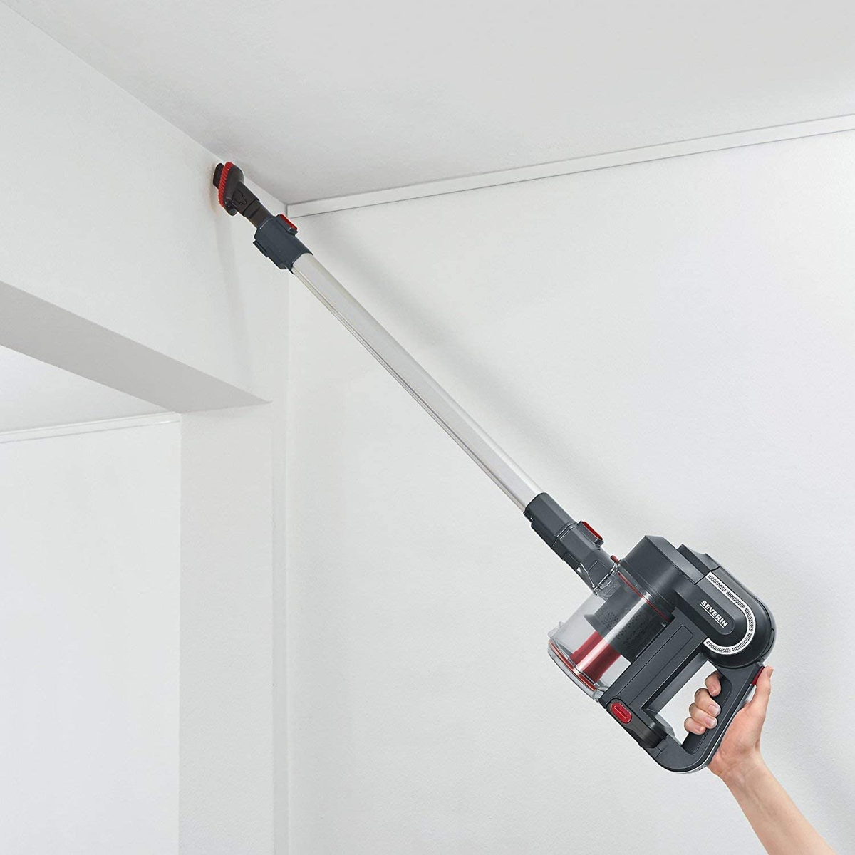 Eine Person saugt eine Wandecke mit einem schwarz-roten Staubsauger. Die Wand ist weiß.