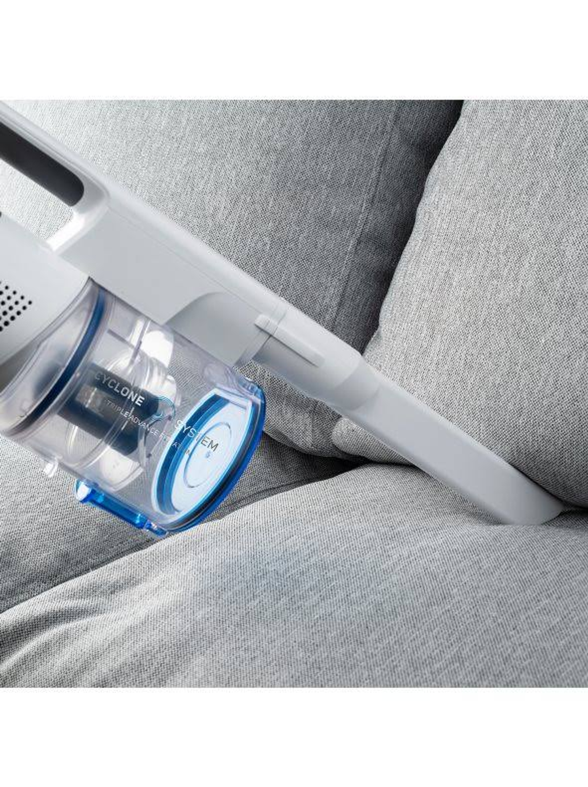 Un aspirapolvere bianco e blu su un divano grigio. L'aspirapolvere è rivolto verso il divano.