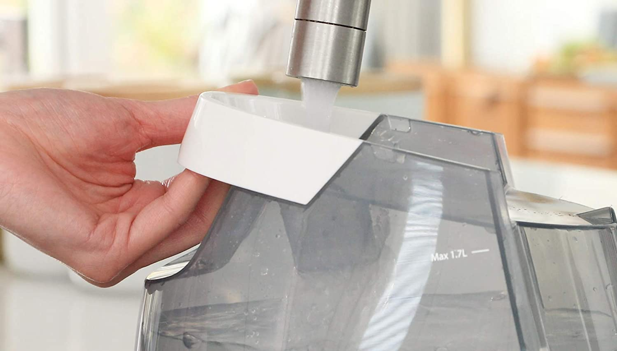 Hand, die einen transparenten Wassertank von einem Wasserhahn befüllt.