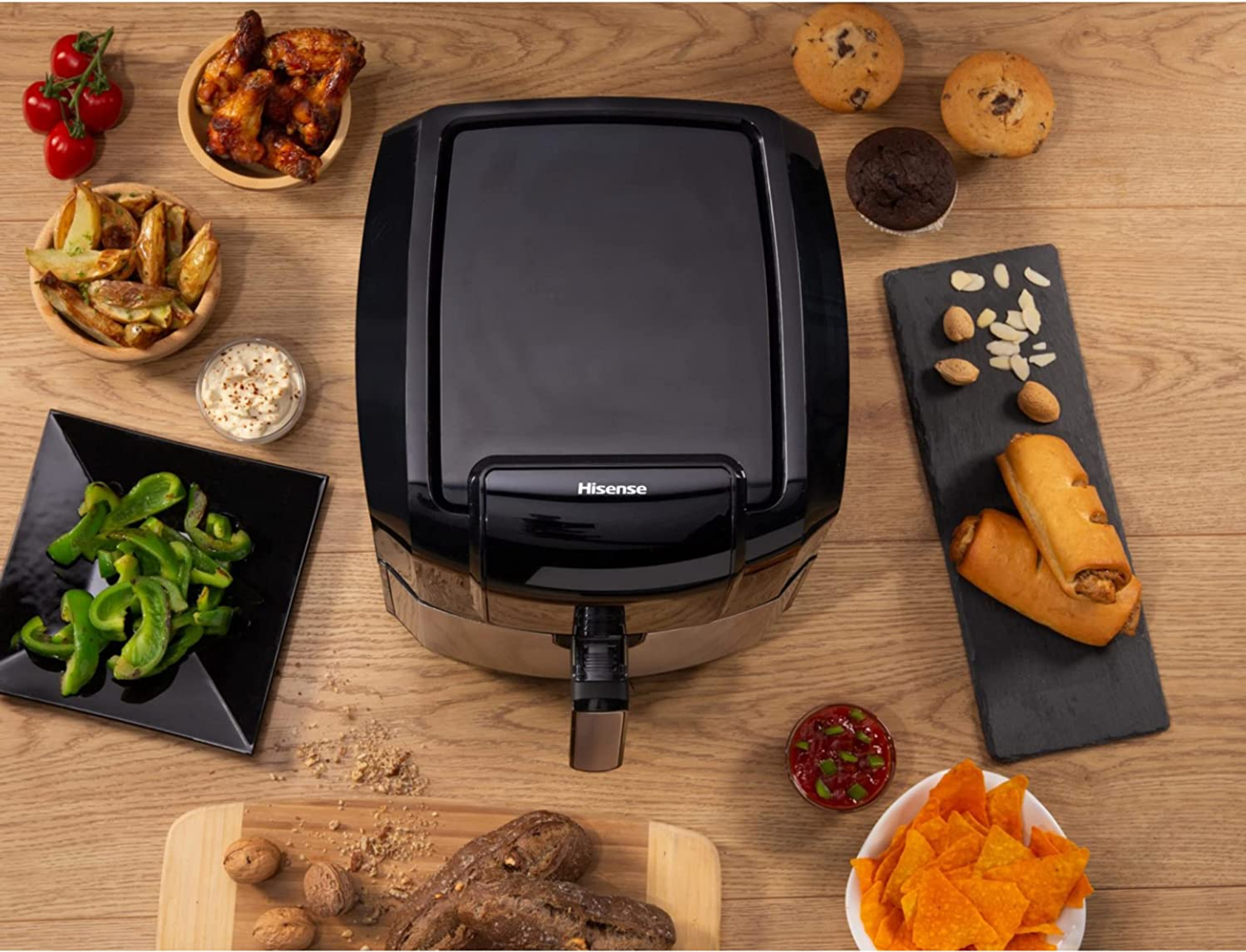 Top view of a black air fryer with food items around it on a wooden table.