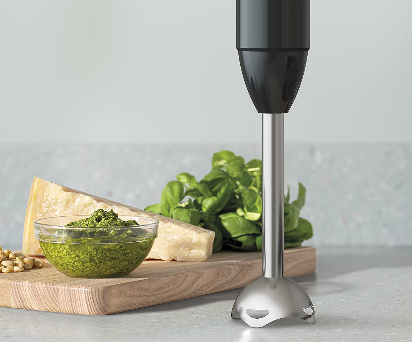 Blender ręczny ze składnikami pesto. Pesto w misce, orzeszki piniowe, ser, bazylia, na drewnie.