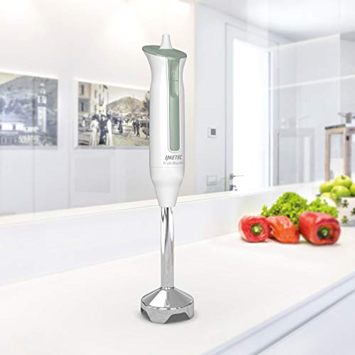 Un frullatore a immersione bianco e verde su un piano di lavoro bianco con verdure.