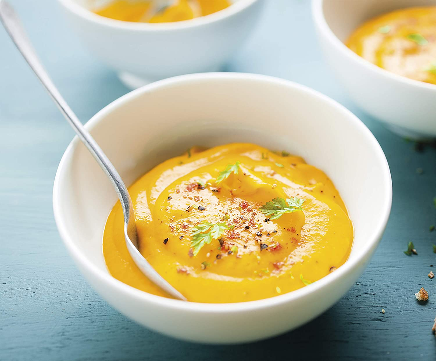 Miska pomarańczowej zupy z łyżką, pietruszką, na niebieskiej powierzchni.