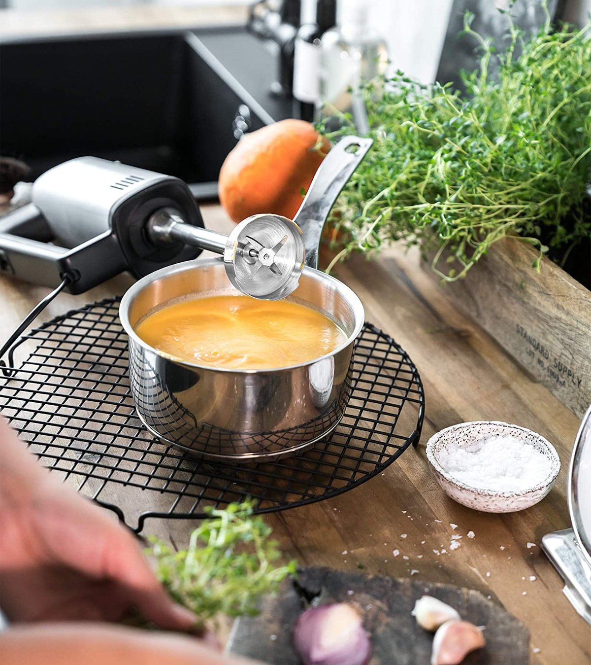 Frullatore a immersione in una pentola con zuppa su una griglia. Ingredienti visibili.