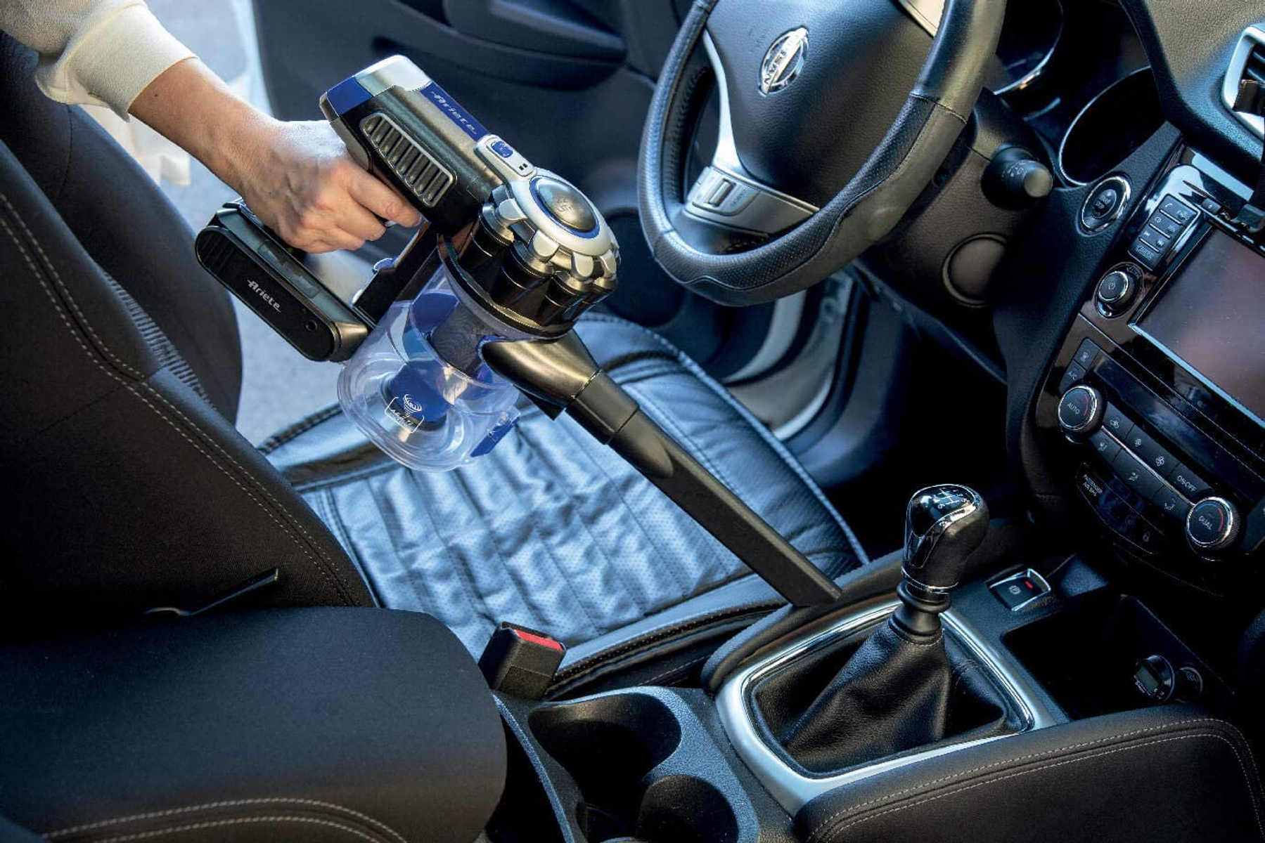 Una mano aspira un sedile dell'auto. L'interno dell'auto include volante e leva del cambio.