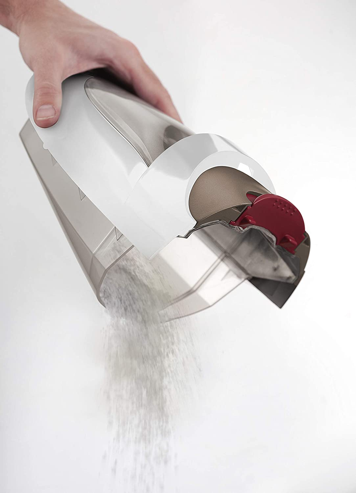 Ręka trzyma pojemnik na kurz z odkurzacza, wysypując kurz. Białe tło.