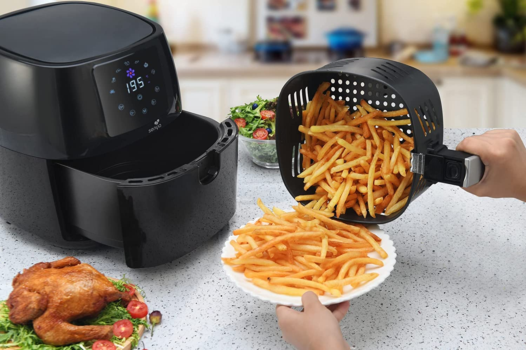 Friggitrice ad aria con patatine versate su un piatto, pollo arrosto e insalatiera su un bancone.