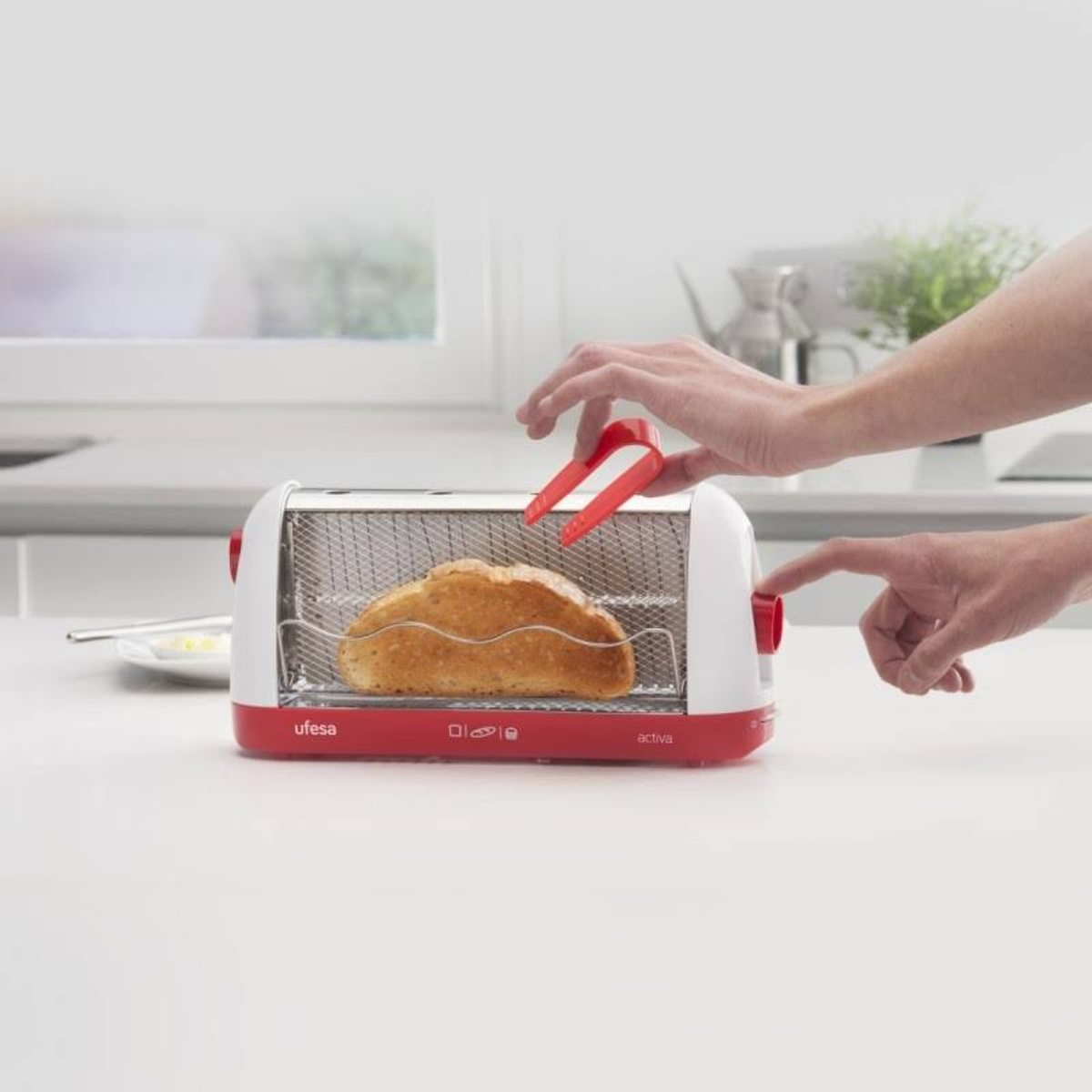 Una persona usa pinzas para sacar tostadas de una tostadora roja y blanca.