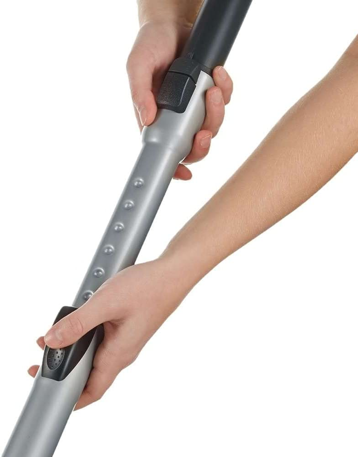 Dłonie trzymające szarą rurę przedłużającą do odkurzacza. Białe tło.