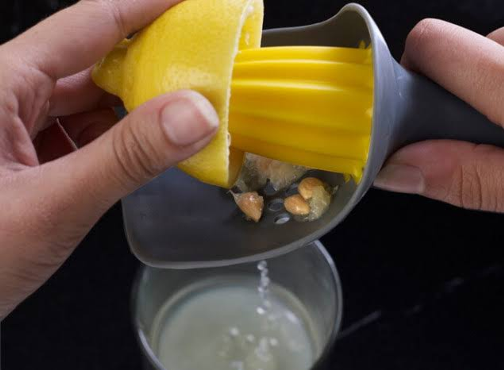 Dłoń wyciskająca sok z cytryny. Sok spływa do szklanki.