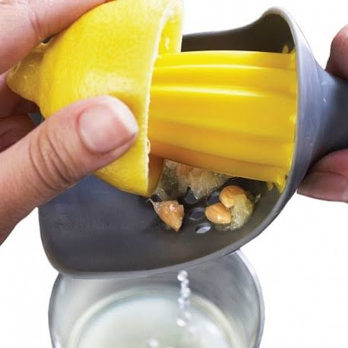 Ręka wyciskająca cytrynę do szarej wyciskarki. Sok i pestki spływają do szklanki.