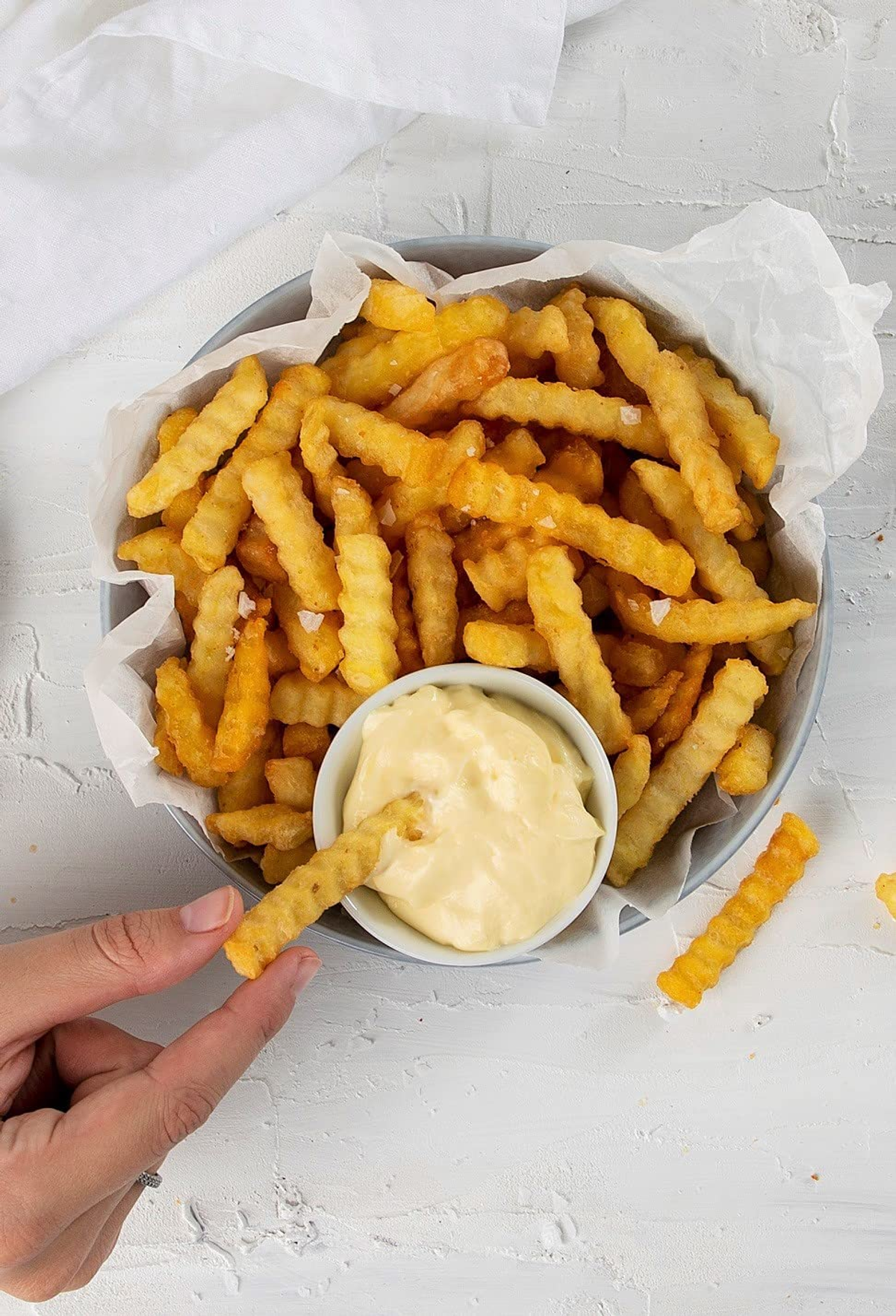 Zbliżenie frytek w misce z dipem, ręka trzyma jedną.