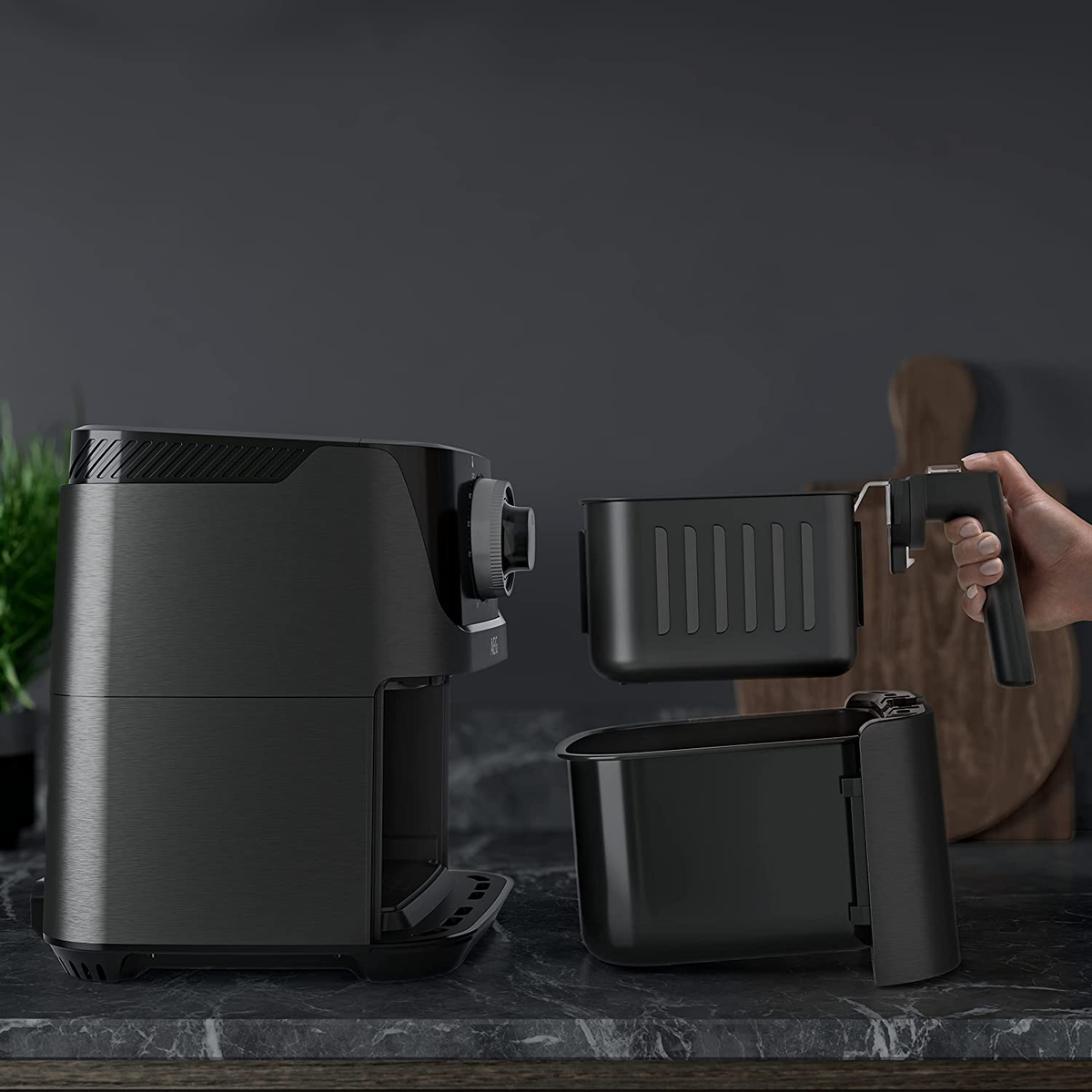 Czarna frytownica powietrzna z dwoma wyjmowanymi koszami na blacie. Ręka trzyma uchwyt kosza.
