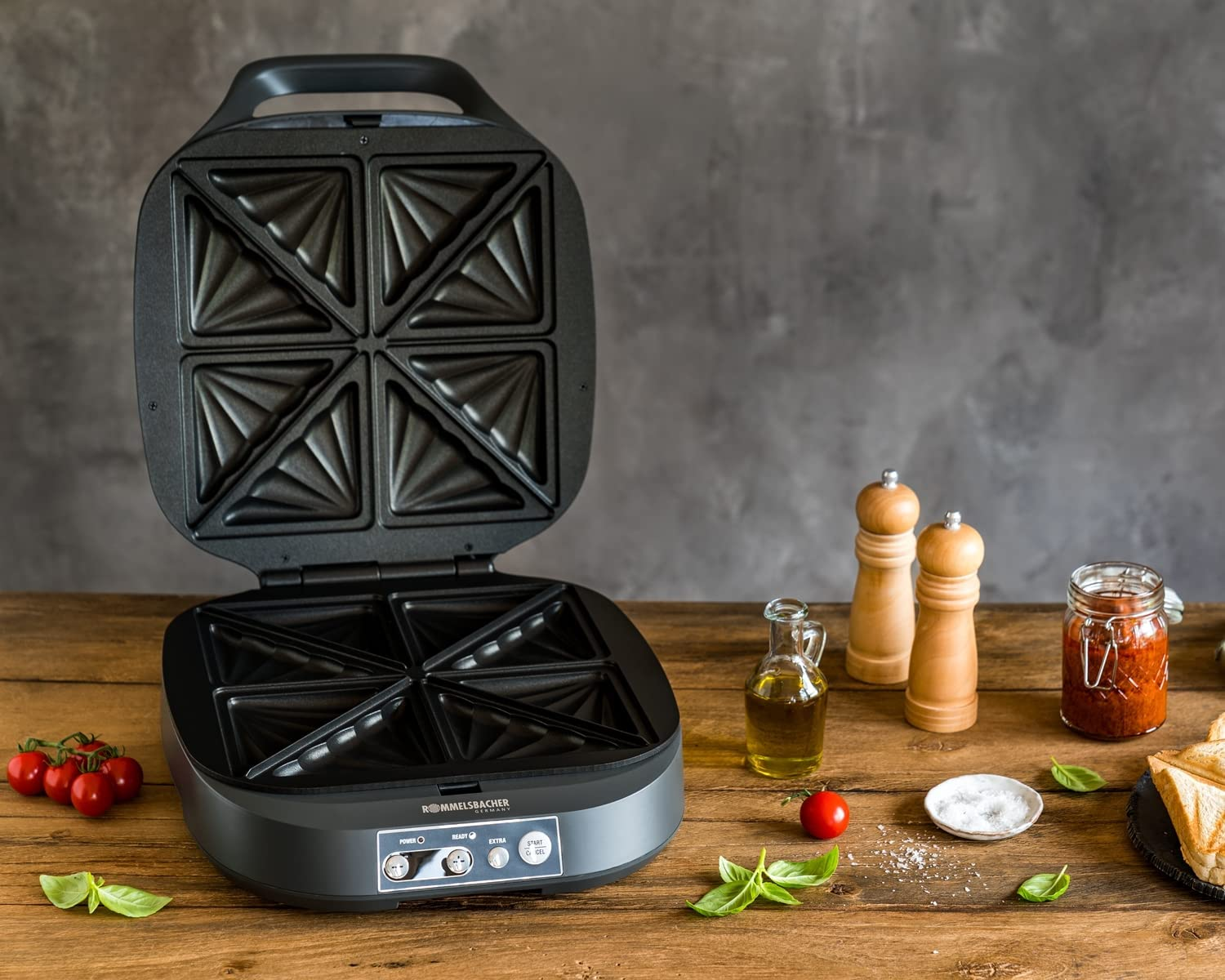 Opiekacz do kanapek, otwarty, pokazujący cztery przegródki. Drewniany stół z jedzeniem.