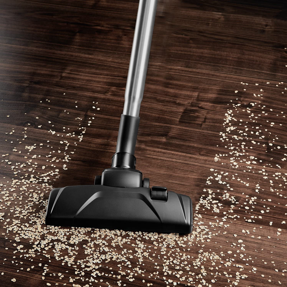 Głowica odkurzacza czyszcząca rozrzucone ziarna na drewnianej podłodze.