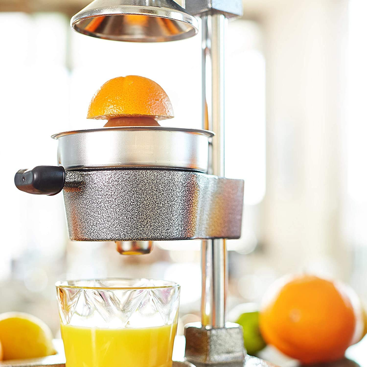 Eine Saftpresse mit einer halben Orange oben, einem Glas Saft und einer Zitrone sichtbar.