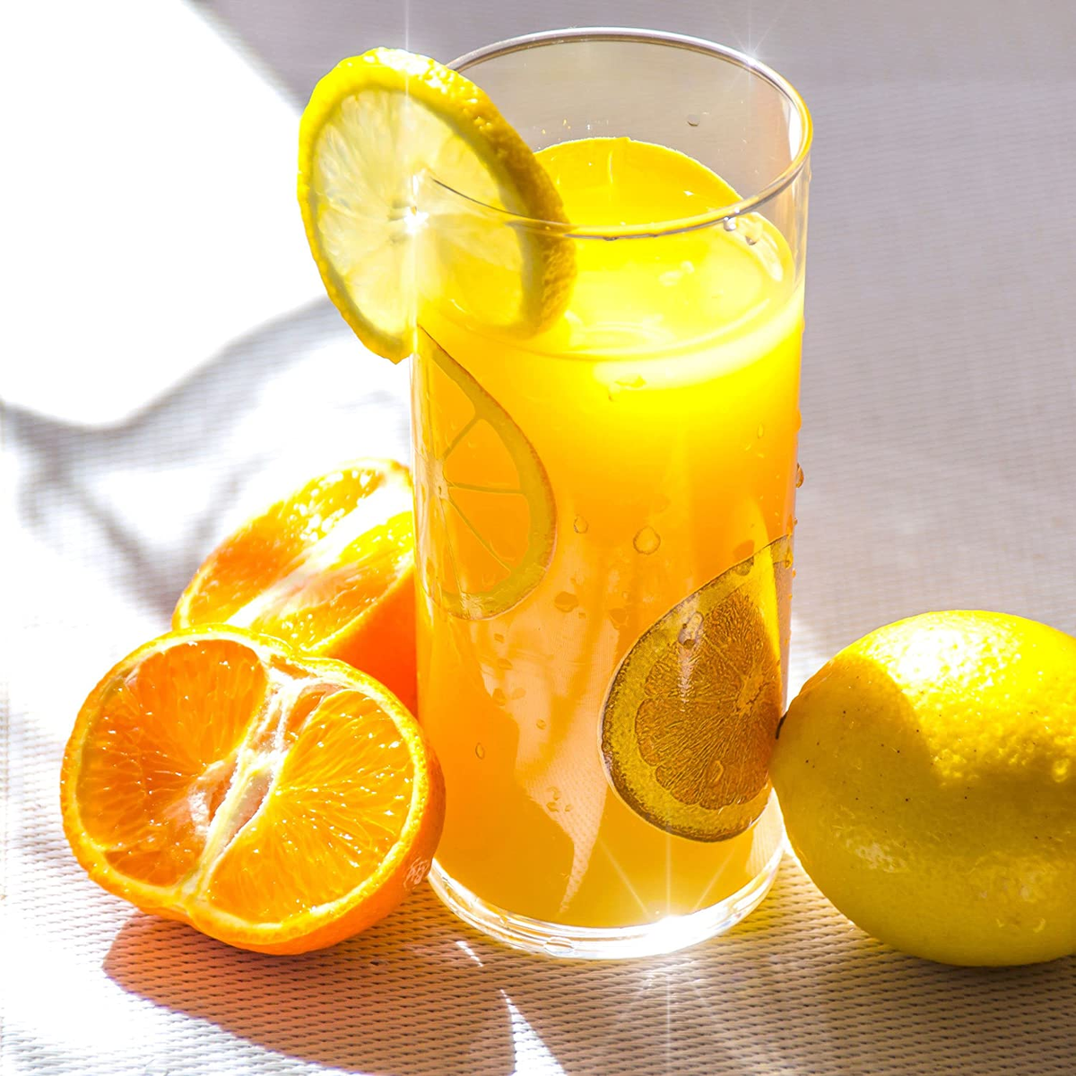 Un bicchiere di succo d'arancia con fette d'arancia e un limone su una superficie bianca.