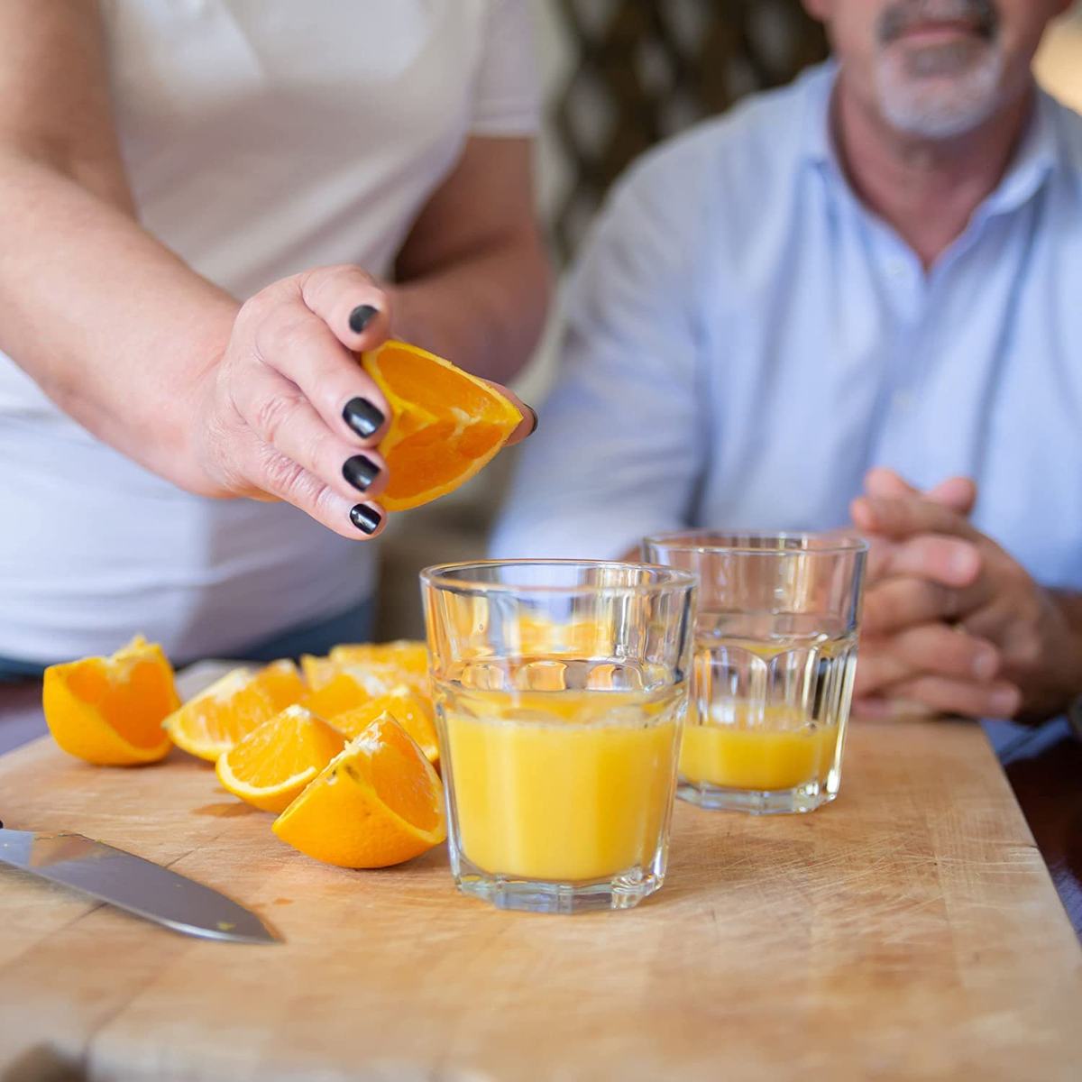 Persona che spremi un'arancia in bicchieri con succo e fette d'arancia.
