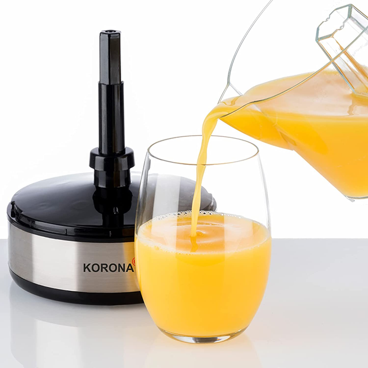 Orangensaft wird aus einer Kanne in ein Glas gegossen.