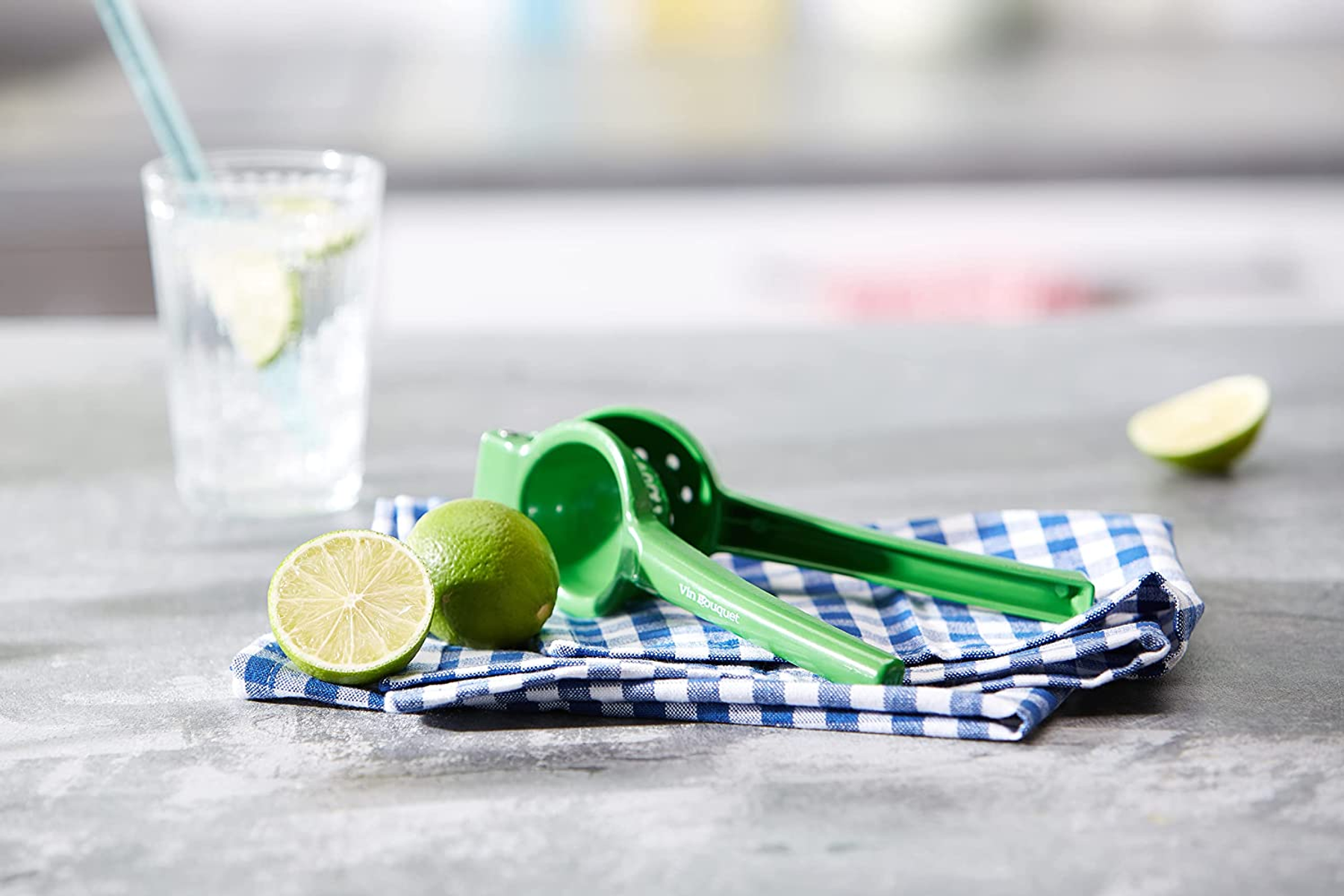 Limette, grüner Entsafter und Getränk mit Strohhalm auf kariertem Tuch.