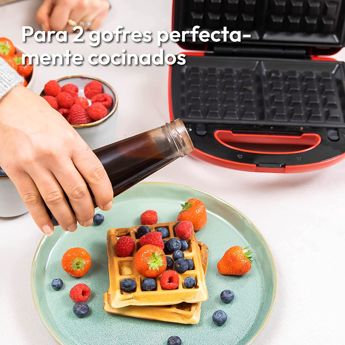 Waffle con frutti di bosco e sciroppo vengono versati. Sullo sfondo una macchina per waffle rossa.