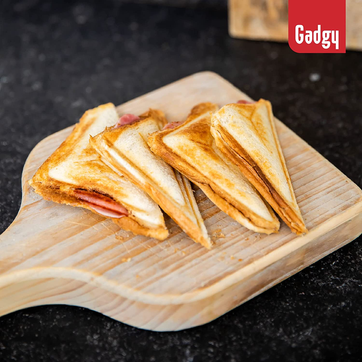 Quattro panini triangolari su un tagliere di legno. I panini sono tagliati a metà e hanno prosciutto all'interno.