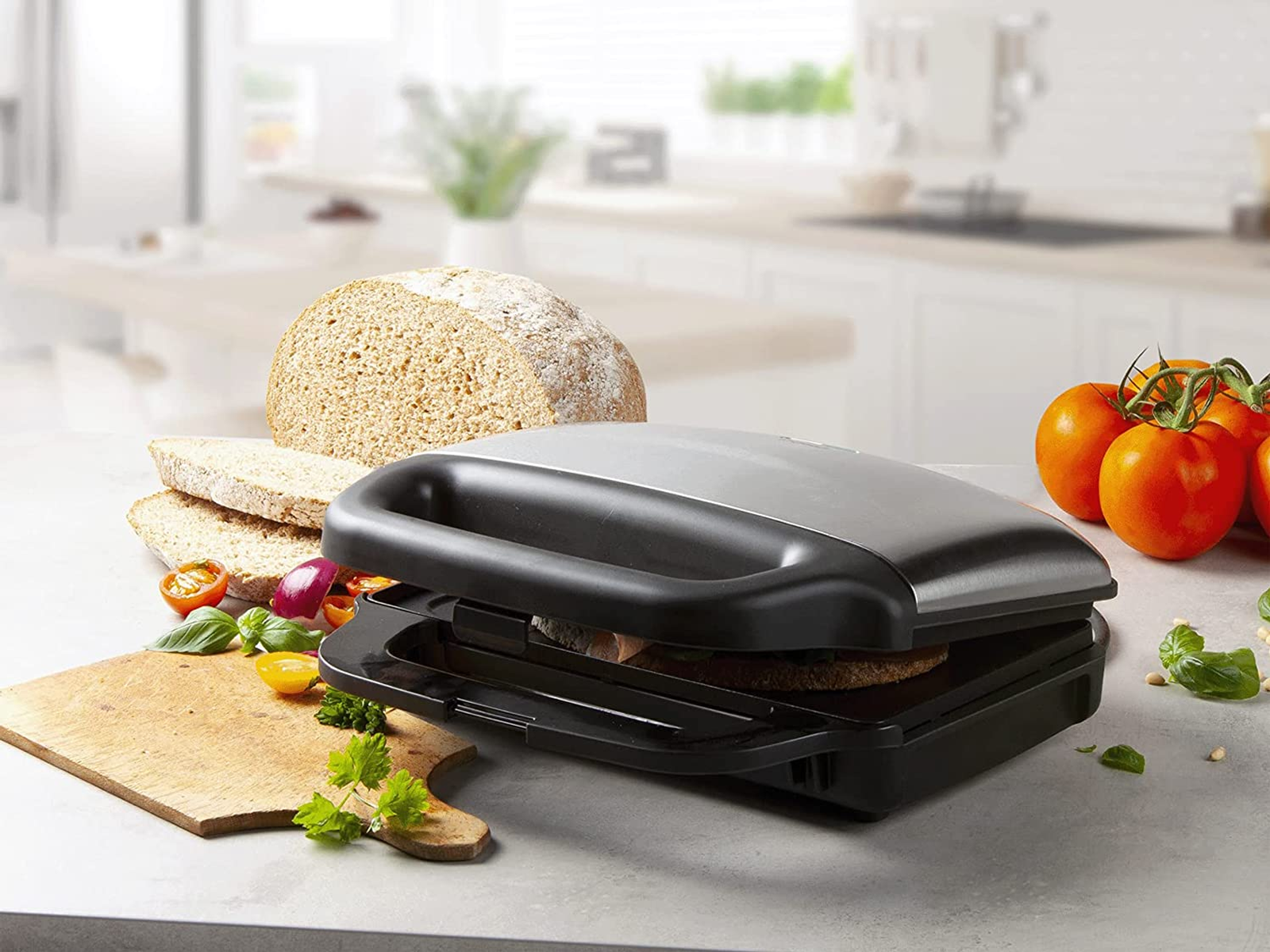 Toster do kanapek z chlebem, pomidorami i bazylią na blacie kuchennym.