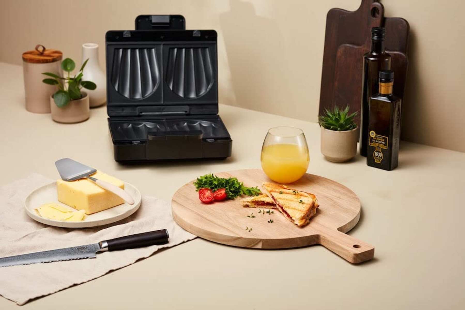 Sandwichmaker, Käse, Brot und andere Lebensmittel auf einer Holzoberfläche. Beigefarbener Hintergrund.