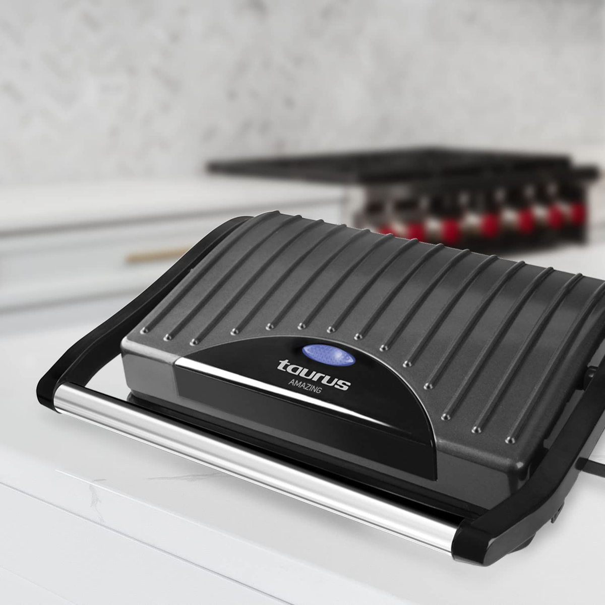 Una plancha para panini negra y gris con una luz de encendido azul y un asa plateada.