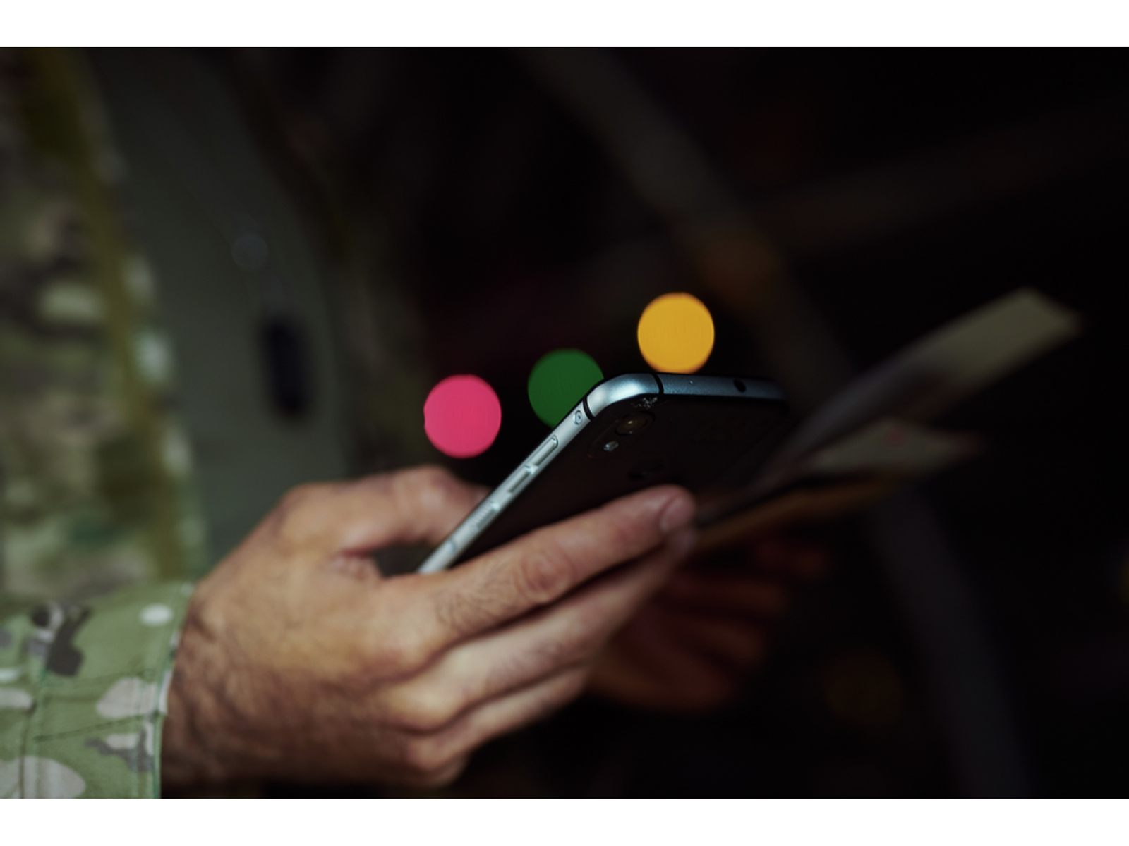 Osoba trzymająca telefon z rozmytym tłem. Trzy kolorowe koła unoszą się nad telefonem.