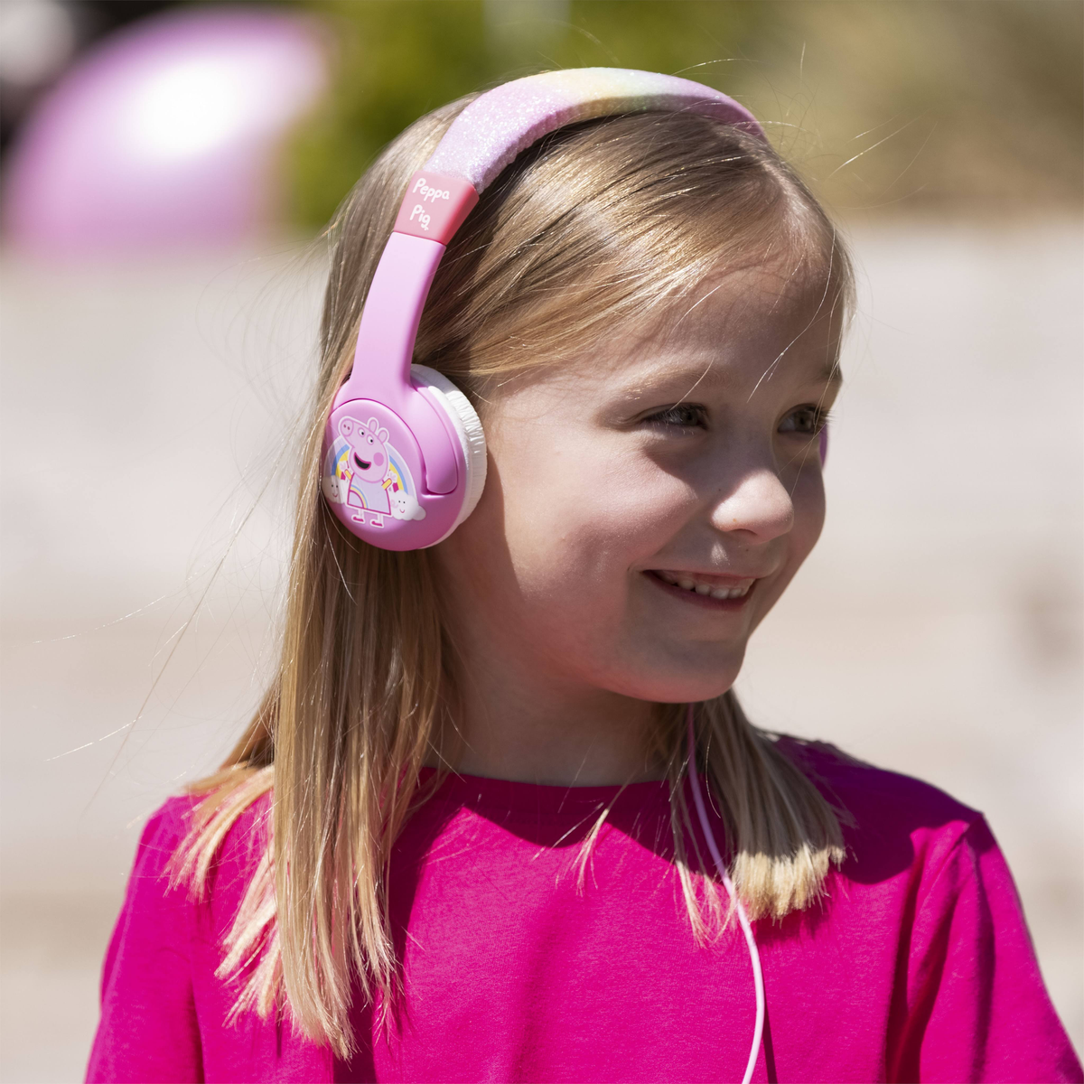 Młoda dziewczyna w różowych słuchawkach Peppa Pig, uśmiechnięta.