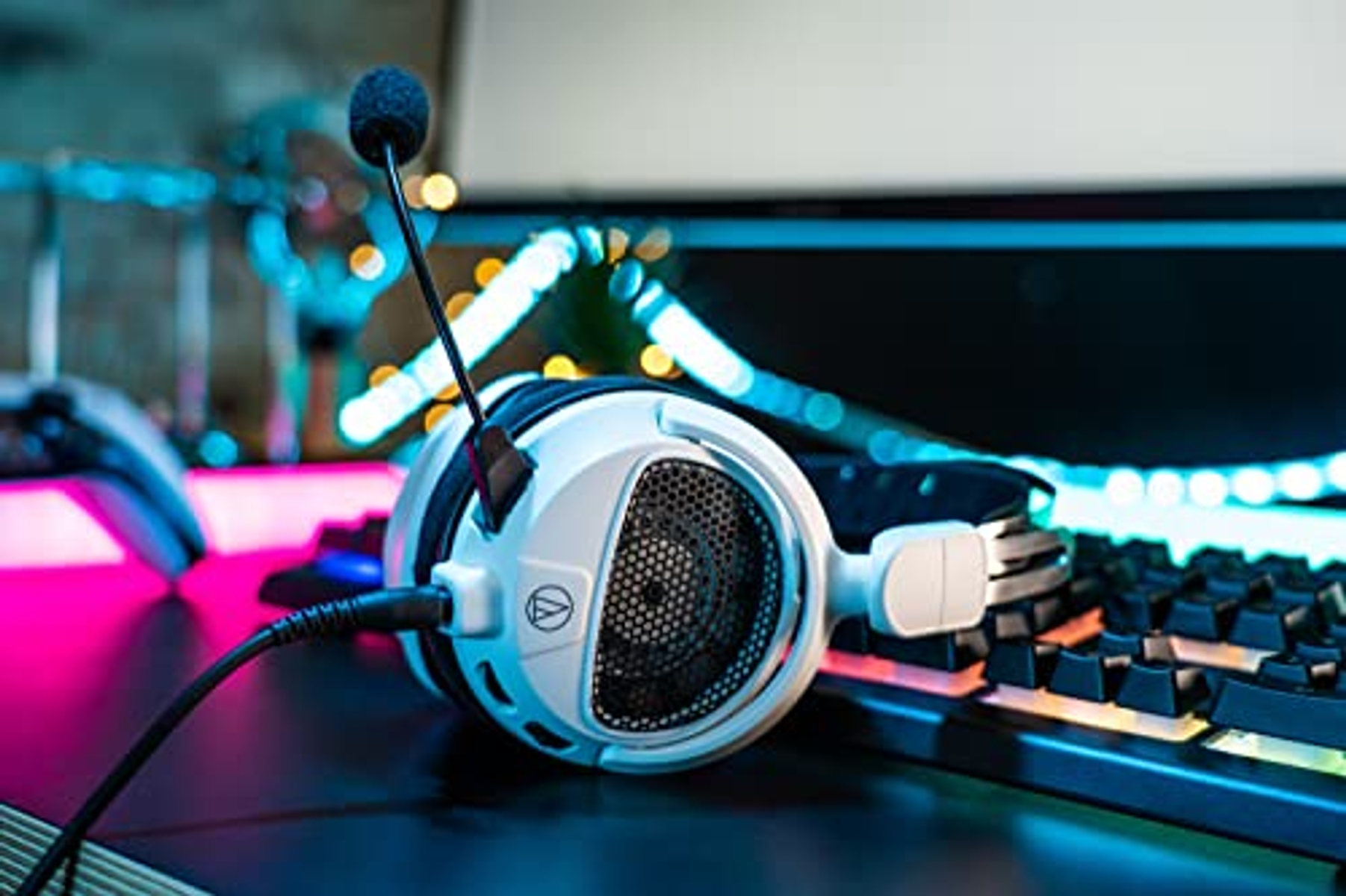 Biały zestaw słuchawkowy dla graczy z mikrofonem, na biurku. Klawiatura i monitor w tle.