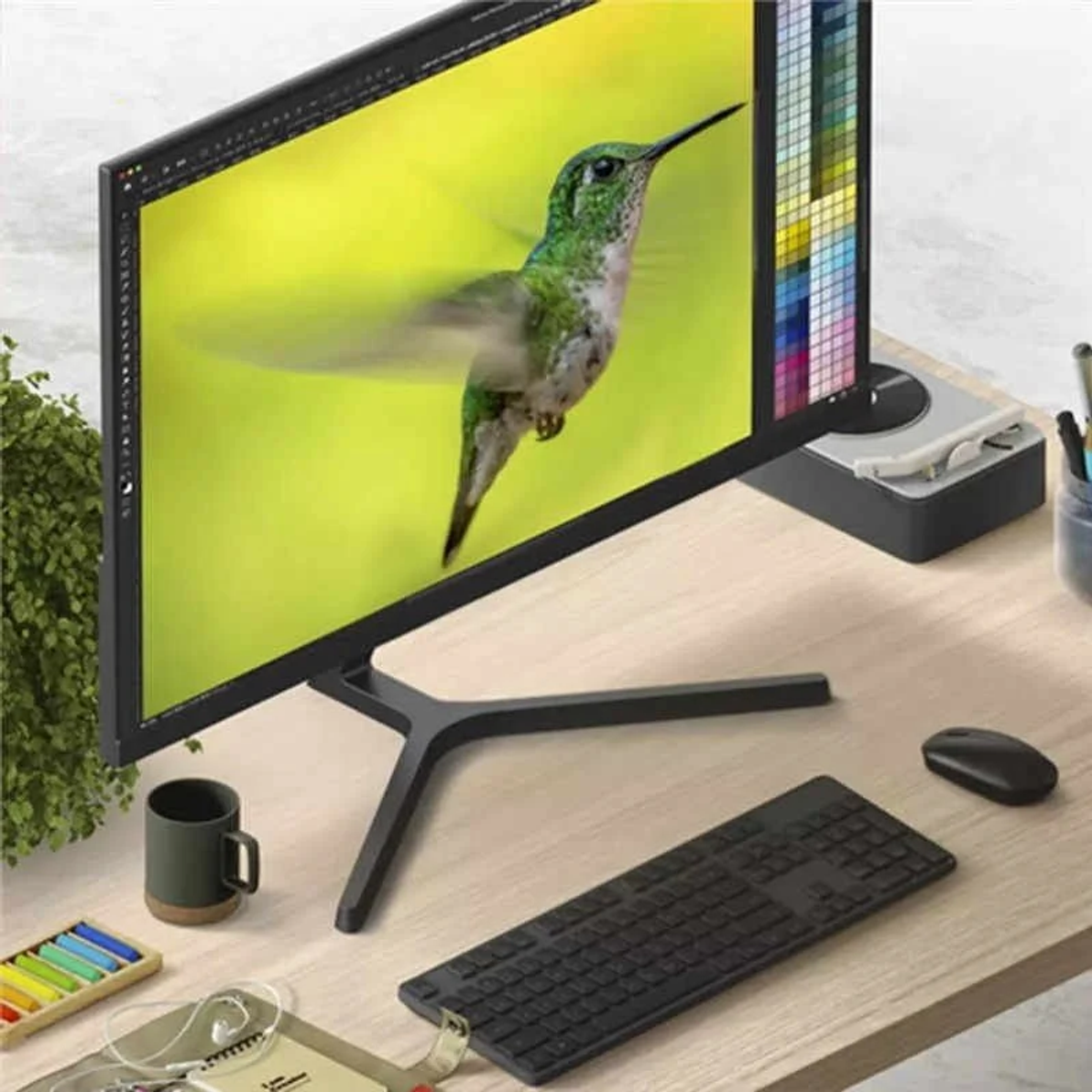 Monitor del computer che mostra l'immagine di un colibrì, con tastiera e oggetti da scrivania.