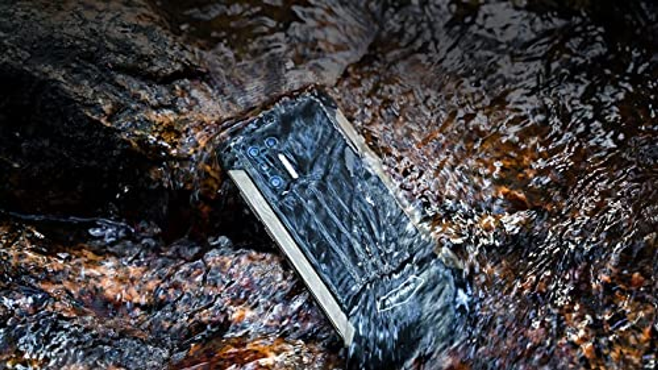 Telefono nero robusto immerso nell'acqua, circondato da rocce.