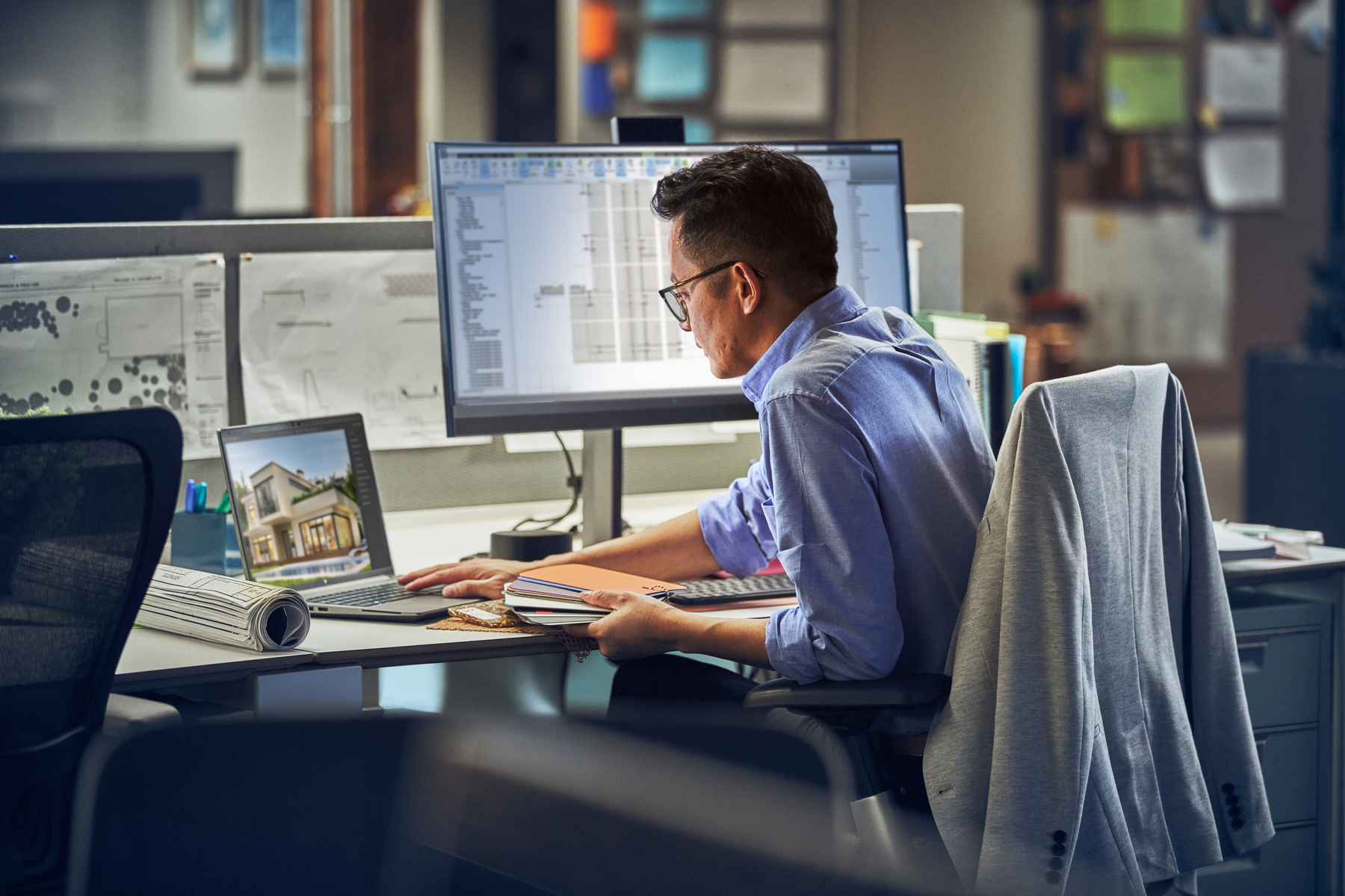 Hombre trabajando en portátil, múltiples monitores y una mesa de dibujo.