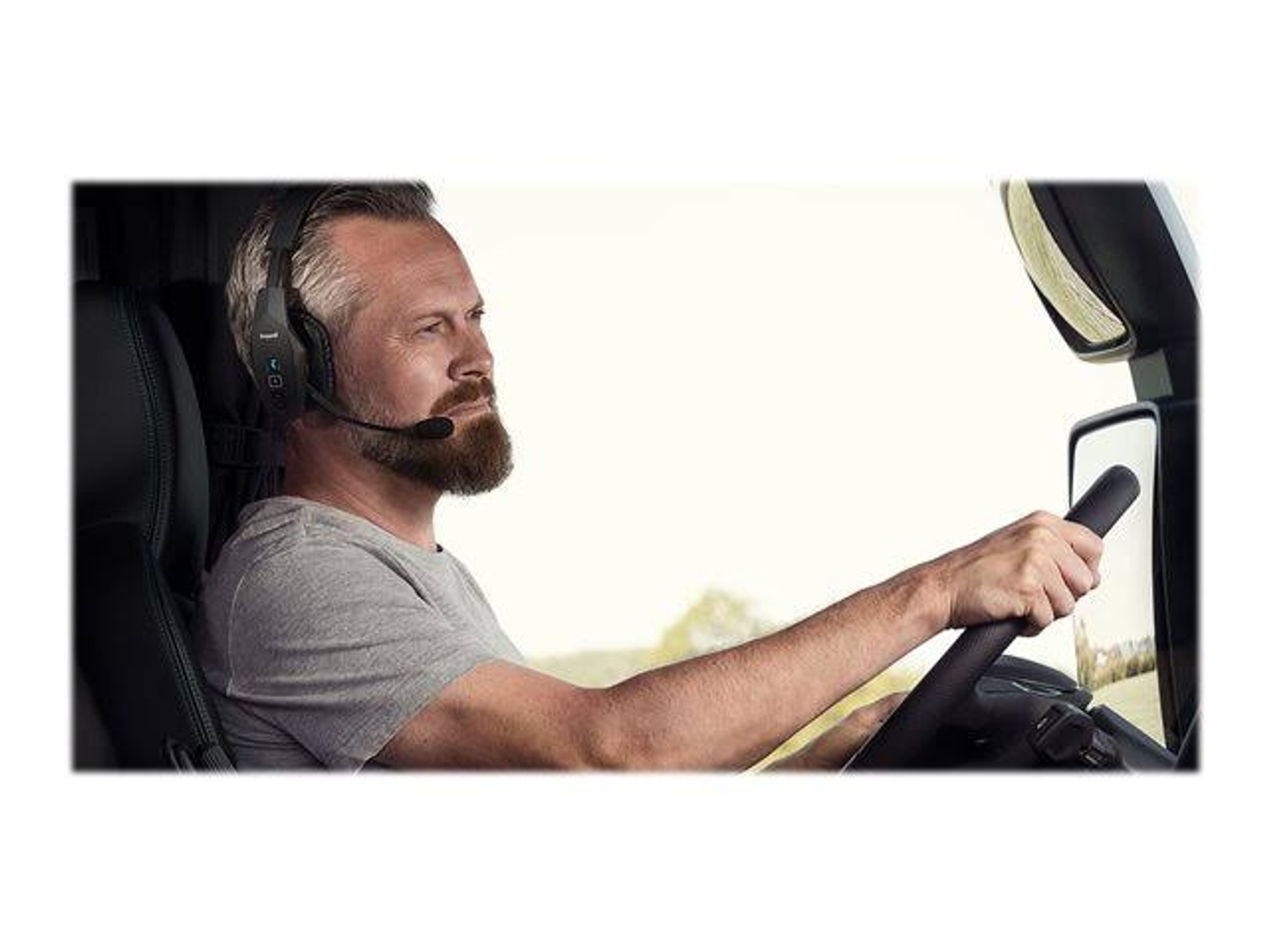 Mężczyzna w kabinie ciężarówki, w zestawie słuchawkowym, patrzący przed siebie, trzymający kierownicę.