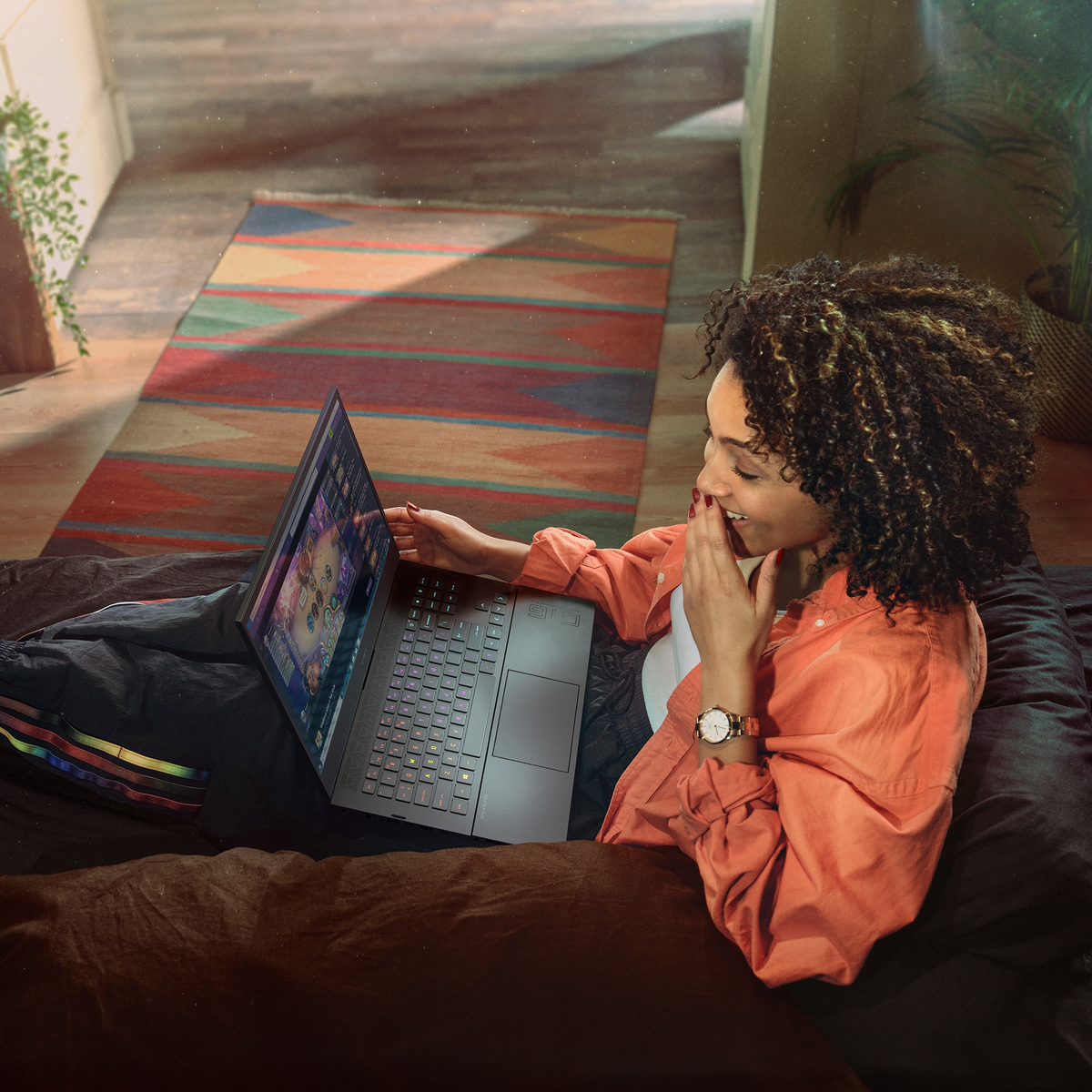 Una mujer usa una laptop en una cama. Un juego colorido está en la pantalla.