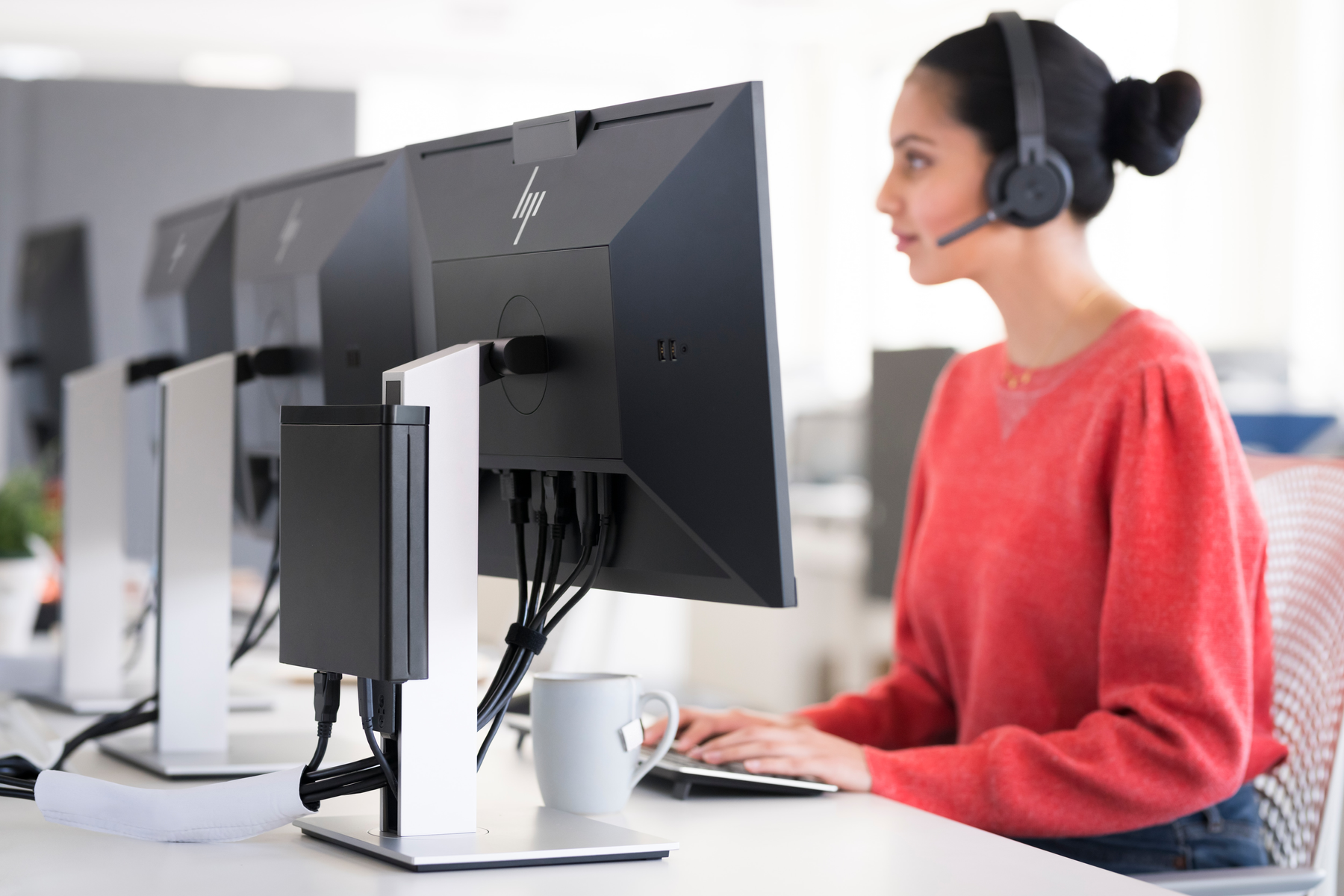 Ustawienia biurowe z kobietą przy komputerze. Monitory są z przodu, a pudełko po lewej.