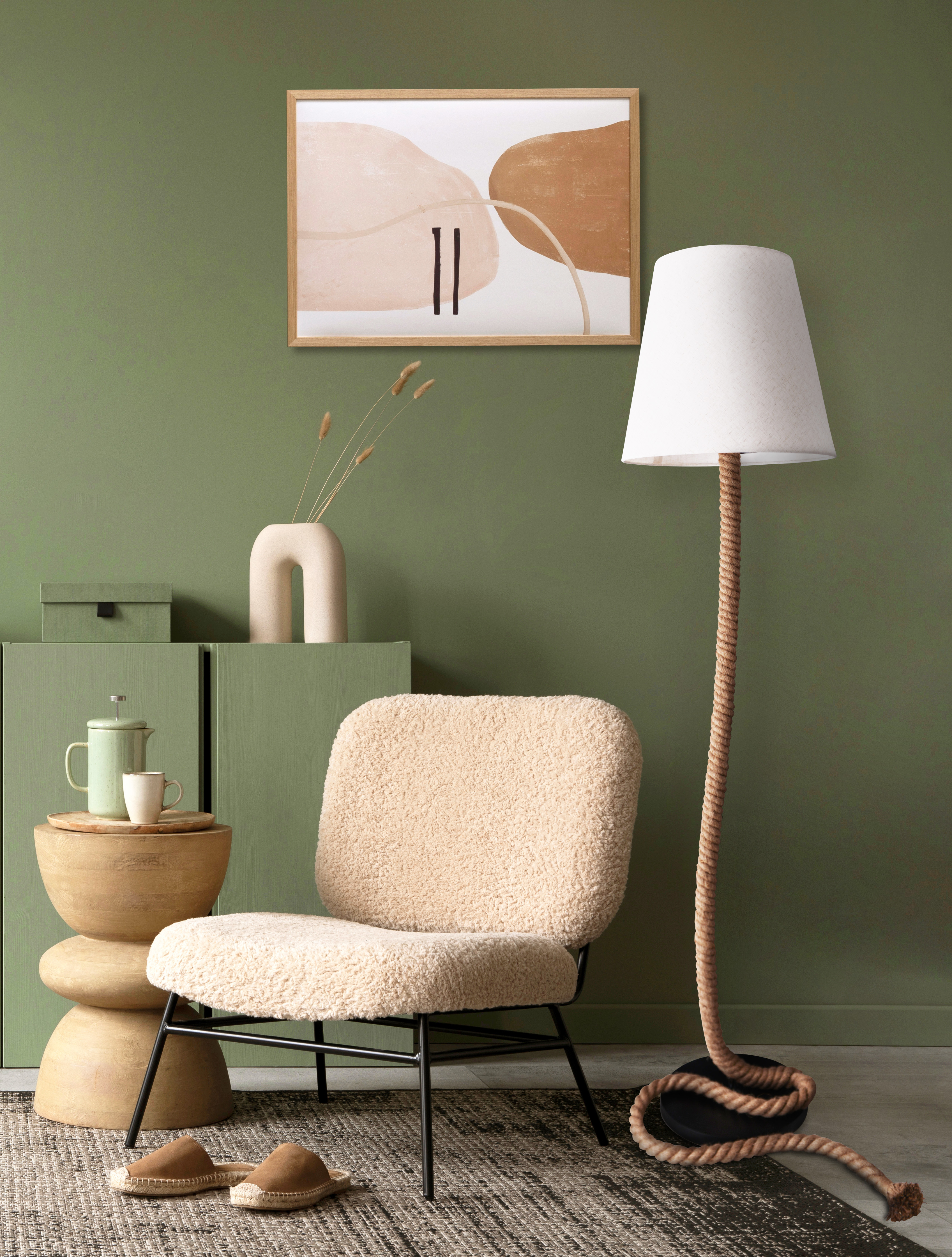 Wohnzimmer mit Stuhl, Tisch, Lampe und einem Gemälde an grüner Wand.