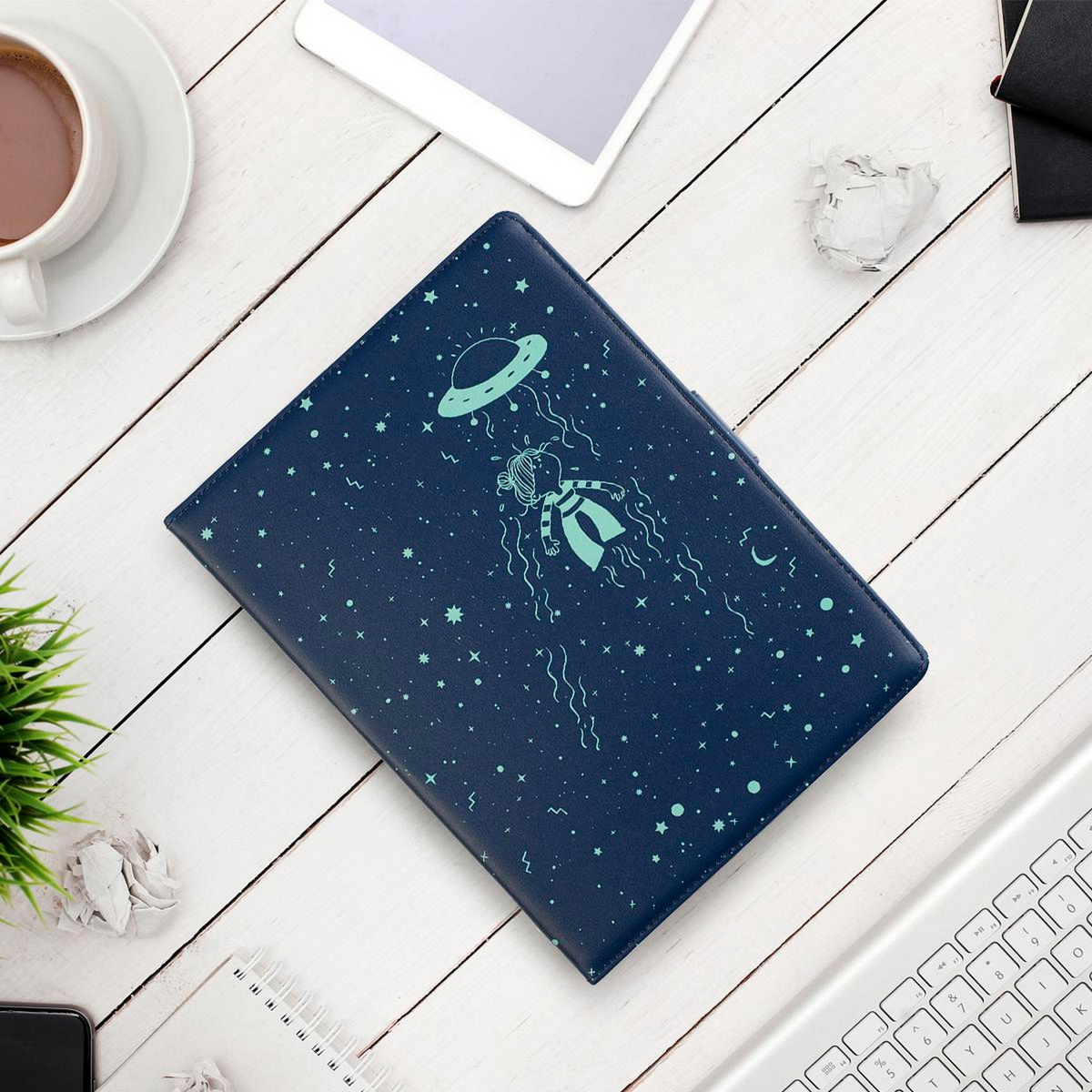Diario azul con un dibujo de una persona en el espacio, rodeada de estrellas y una tableta.
