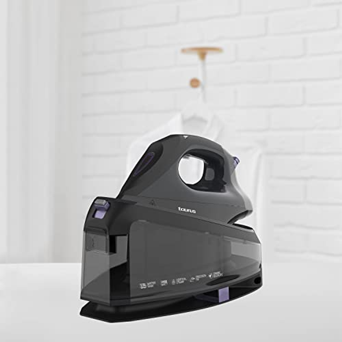 Schwarzes Bügeleisen auf einem weißen Tisch, mit Kleidung im Hintergrund.